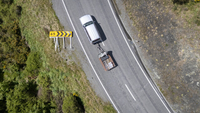 Aerial view of a silver car and trailer passing a storm felled road warning sign, contrasted against the lush greenery, Hanmer Springs, Canterbury Region, New Zealand.