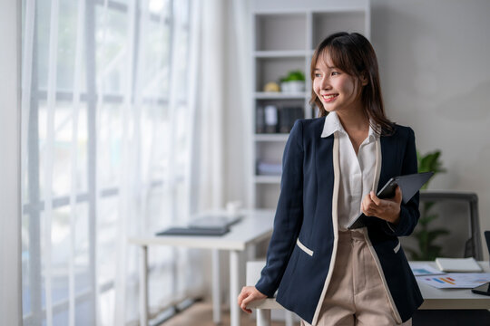 Young asian businesswoman smiling and holding tablet in modern office - Powered by Adobe
