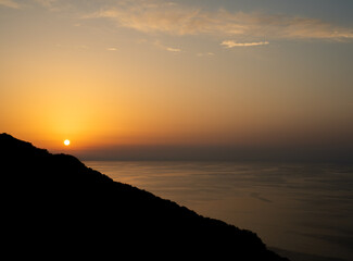 Golden sunset over the Mediterranean Sea, with a silhouetted hillside and calm water horizon in Sicily, Italy.