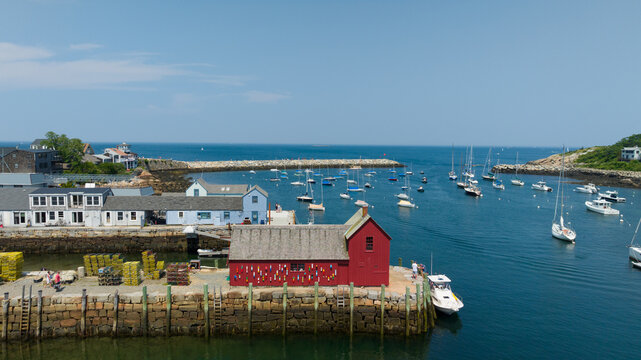 Aerial view of Motif Number 1, a vibrant red fishing shack, contrasted with the tranquil blue harbor and ocean dotted with boats. Rockport, Massachusetts, USA.