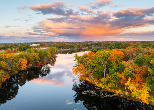 Aerial view of Fisk Pond with a vibrant tapestry of fall foliage under a dramatic sunset. Natick, Massachusetts, USA.