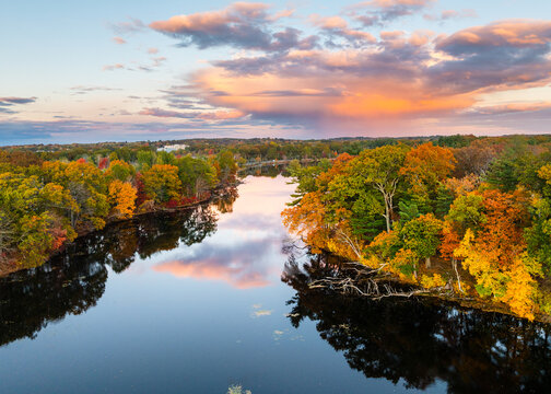 Aerial view of Fisk Pond with vibrant autumnal foliage, reflecting the colorful sunset in its waters. Natick, Massachusetts, USA.