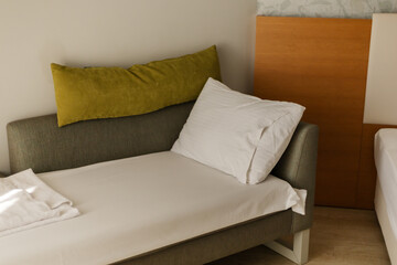 A cozy space features a minimalist bed with white linens and a grey sofa adorned with green throw pillows, creating a serene atmosphere perfect for relaxation