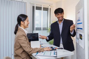 Business colleagues are engaged in a collaborative discussion, analyzing financial charts and reports on the wall and table. They exchange ideas, review strategies, and plan future goals.