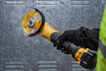 Close-up of a worker using a yellow angle grinder with spinning disc. Builder wearing safety gloves and vest. Concept of construction, metalworking, and industrial power tools in action.