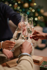 Multiethnic group of young adult men and women clinking champagne glasses together in celebration, hands visible in foreground with festive decorations in background