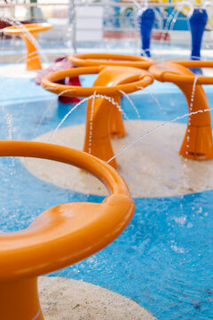 Children can enjoy playtime in a lively splash pad featuring colorful water structures. Bright orange fountains spray water, creating a playful atmosphere on a sunny day