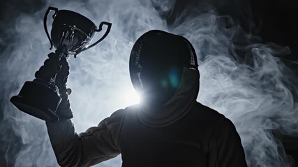 Silhouette fencer standing triumphantly with trophy in dramatic smoky atmosphere. Victory pose after fencing match. Champion celebration concept in sports footage