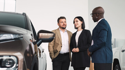 Group of diverse individuals discussing car features at a dealership, showcasing a modern vehicle, emphasizing the buying experience and customer engagement in automotive sales