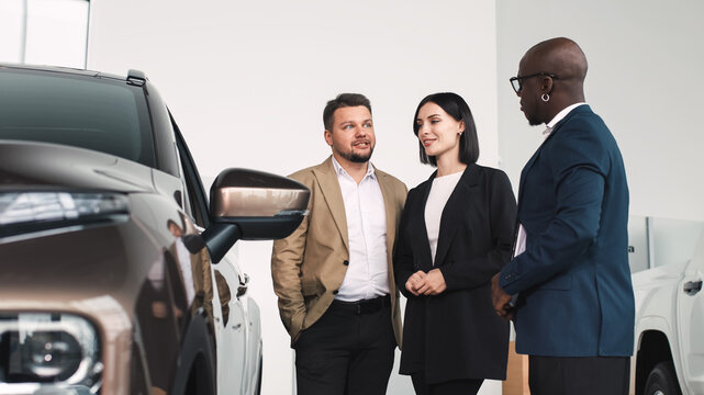 Group of diverse individuals discussing car features at a dealership, showcasing a modern vehicle, emphasizing the buying experience and customer engagement in automotive sales