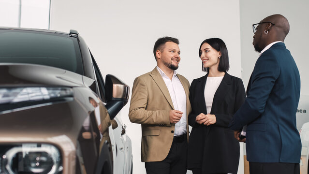 A young couple chatting in a car dealership, discussing car options and features, demonstrating their car buying and customer service experience.