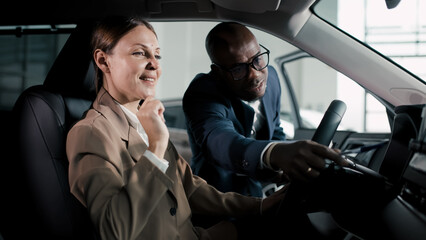 Professional woman in beige suit smiles while exploring car features with a salesman in a...