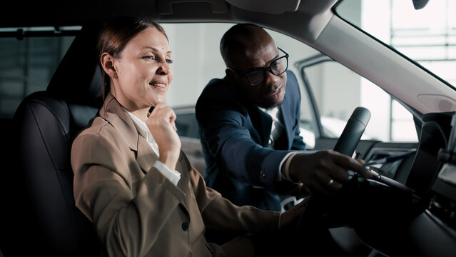 Professional woman in beige suit smiles while exploring car features with a salesman in a dealership, showcasing the car buying experience and customer service - Powered by Adobe