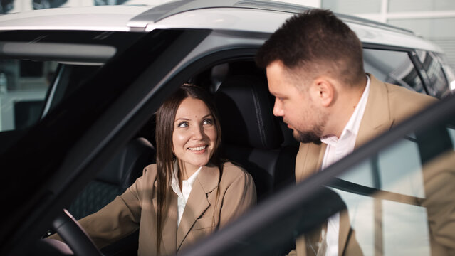 Smiling woman and man in beige suits discussing car features inside dealership vehicle, showcasing customer experience and engagement in car buying process