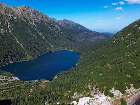 Aerial view of Morskie Oko lake's deep blue waters nestled between the rugged, green-clad slopes of the Tatra Mountains under a clear sky, Morskie Oko, Lesser Poland Voivodeship, Poland.