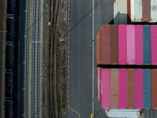 Aerial view of cargo containers casting long shadows beside train tracks, a stark contrast of industrial colors and geometric shapes, Berlin, Germany.