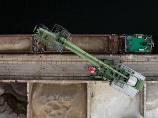 Aerial view of a crane loading raw materials from a barge onto a dock, showcasing the industrial activities along the river, Berlin, Germany.