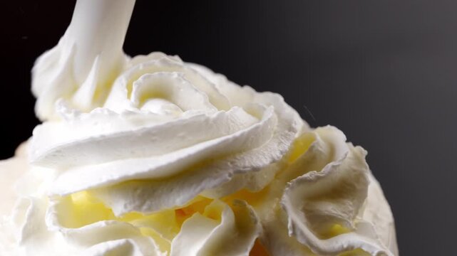 Whipped cream is squeezed out of a can onto a rotating cup of coffee. preparation of delicious invigorating and dessert drinks. black background.