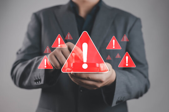 Businessman holding smartphone with red warning alert icons, symbolizing cybersecurity threat, phishing attack, data breach, malware infection, and digital risk management in modern business. - Powered by Adobe