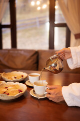 Relaxing tea time in a cozy lounge area after sauna session, with cups of tea, teapots and desserts on a wooden table near window in warm interior.