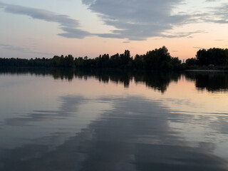 Calm evening scene over a tranquil lake reflecting soft sunset colors and silhouetted trees during late summer