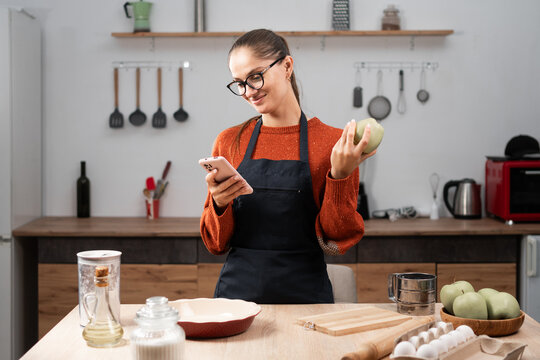 Portrait of woman wearing apron cooking apple pie enjoy making clean food reading recipe online using smartphone in kitchen at home. baking, cookies and dessert.