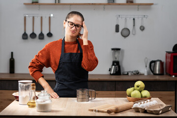 Young housewife baker woman wears apron suffering headache and migraine in the kitchen. Medicine, healthcare and Cooking food