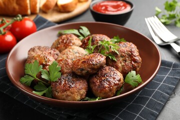 Delicious patties with parsley in bowl on dark textured table, closeup