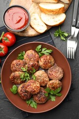 Delicious patties with parsley in bowl, tomatoes, bread and ketchup on dark textured table, flat lay