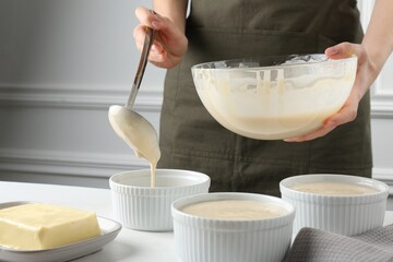 Woman pouring batter (liquid dough) into baking dishes at table indoors, closeup