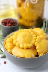 Pickled pattypan squashes in bowl on white tiled table, closeup