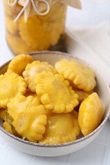 Pickled pattypan squashes in bowl and jar on white tiled table, closeup