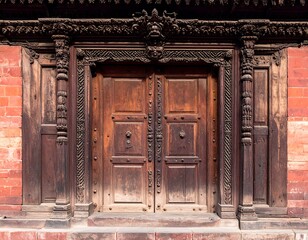 Ornate wooden doorway framed by pillars against a red brick wall
