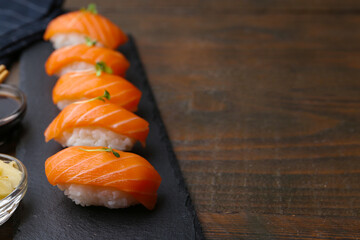 Delicious nigiri sushi with salmon and microgreens on wooden table, closeup. Space for text