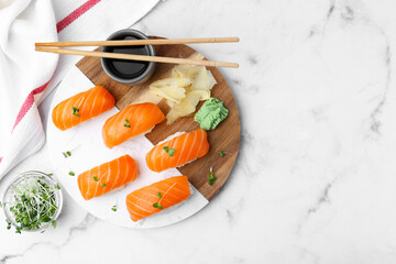 Delicious nigiri sushi with salmon, microgreens, ginger, wasabi, soy sauce and chopsticks on white marble table, flat lay. Space for text