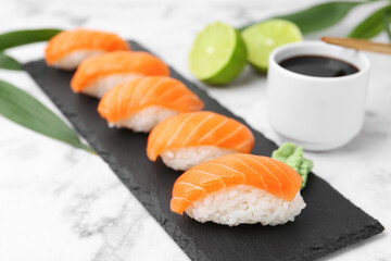 Delicious nigiri sushi with salmon, wasabi, lime and soy sauce on white marble table, closeup