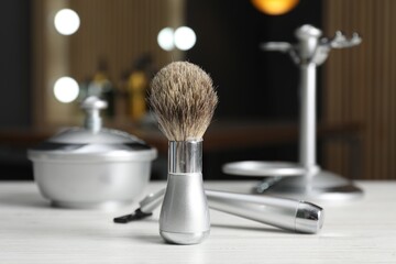Shaving brush and other barber's tools on light wooden table in barbershop, closeup