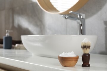 Shaving brush and foam on white counter near sink in bathroom. Barber's tools