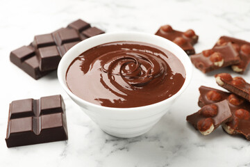 Bowl with melted chocolate and pieces on white marble table, closeup