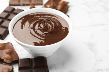 Bowl with melted chocolate and pieces on white marble table, closeup. Space for text