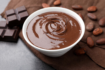 Bowl with melted chocolate, beans and pieces on grey table, closeup