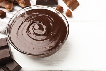 Melted chocolate and pieces with hazelnuts on white wooden table, closeup. Space for text