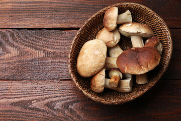 Fresh porcini mushrooms in wicker basket on wooden table, top view. Space for text