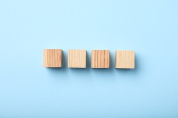 Wooden cubes on light blue background, top view