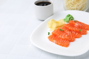 Fresh salmon sashimi with microgreens, wasabi, ginger and soy sauce on light tiled table, closeup. Space for text