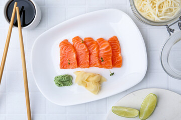 Fresh salmon sashimi with microgreens, wasabi, ginger and soy sauce served on light tiled table, flat lay