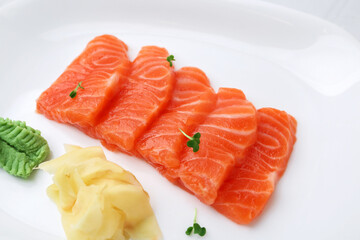 Fresh salmon sashimi with microgreens, wasabi and ginger on white plate, closeup