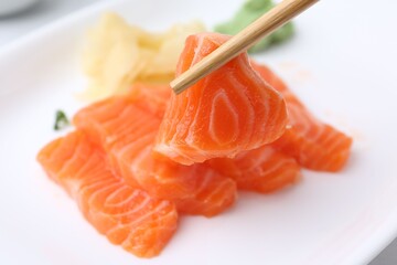 Taking fresh salmon sashimi with chopsticks from plate, closeup