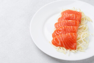 Fresh salmon sashimi with sliced radish on light grey table, closeup. Space for text