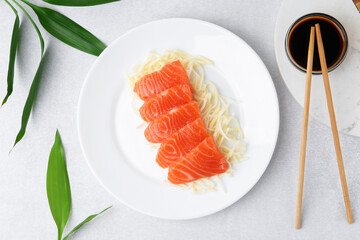 Fresh salmon sashimi with sliced radish and soy sauce on light grey table, flat lay